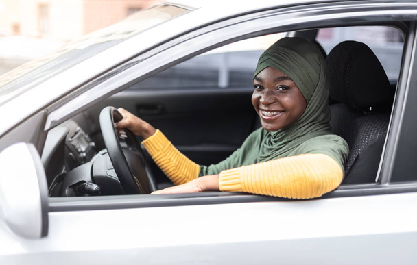 Car Insurance Concept. Smiling african muslim woman sitting in modern vehicle - Photo, Image