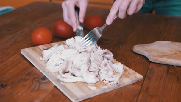 Mujer corta filete de pollo cocido a mano en una tabla de cortar con un tenedor y un cuchillo. - Imágenes, Vídeo
