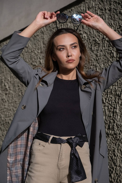 atraente jovem asiático modelo no cinza trincheira casaco de pé perto da parede ao ar livre - Foto, Imagem