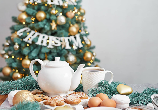 Kersttafel gedekt. Snoepgoed en eten. Theeset en snoepjes op achtergrond van kerstboom. Kerstviering. Wintervakantie. Kerst maquette. Sjabloon wenskaart - Foto, afbeelding