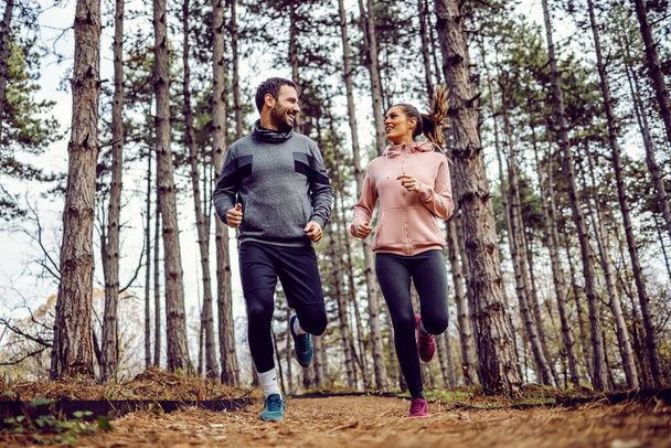 Plná délka veselý mladý pár ve sportovním oblečení běží v přírodě. Zdravý životní styl koncept. - Fotografie, Obrázek