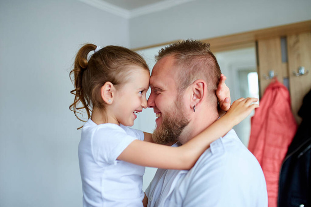 Adorable little girl in white dress hugging loving father looking at him with love and tenderness, Father and daughter spending time at home. Happy Father's Day, I love you, dad. - Photo, Image