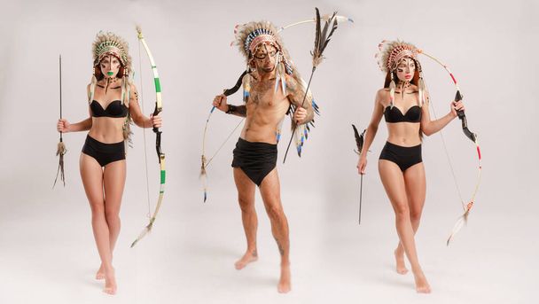 egy férfi és egy nő az amerikai őslakos népek képében, íjjal és nyíllal fehér alapon pózol. - Fotó, kép