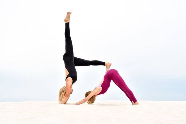 Two beautiful young women practice steamy yoga on the beach - Valokuva, kuva