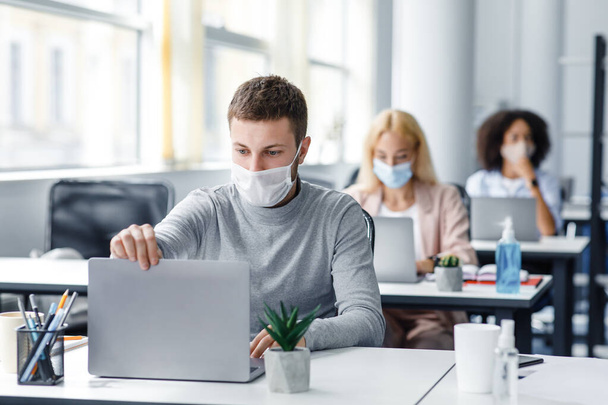Coronavirus quarantine and office work with colleagues keeping social distancing. Portrait of young man in protective mask make video call with client - Photo, Image