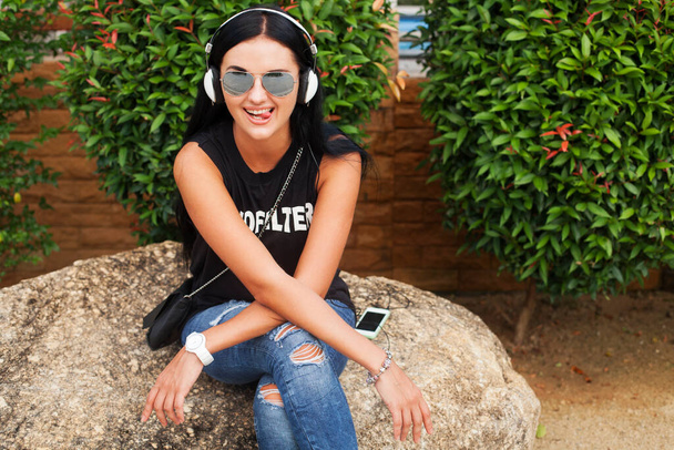 young stylish hipster woman in black t-shirt, jeans, listening to music on headphones, having fun, posing, funny, smiling - Foto, Imagen