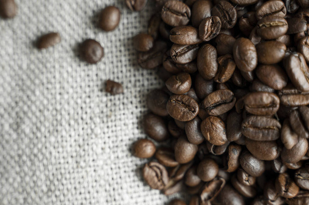 Coffee beans on a linen textile and on a wooden table background. Fresh arabica coffee beans. - Фото, изображение