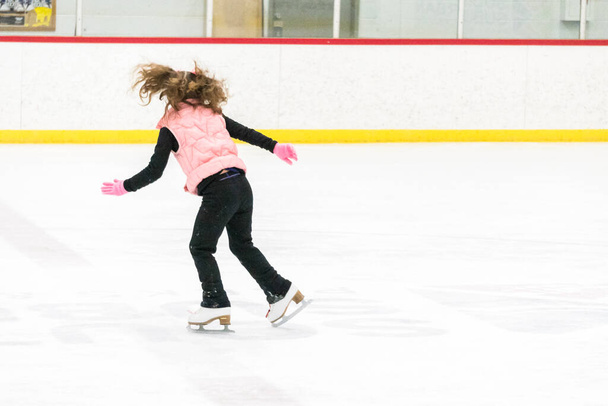 Niña practicando movimientos de patinaje artístico en la pista de hielo interior. - Foto, imagen