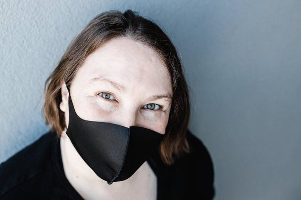 Kaukasische Frau mit schwarzer Maske während der COVID-19 Coronavirus-Pandemie - Foto, Bild