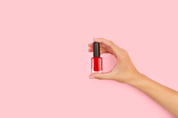 Woman hand holding a red nail polish on a pink background with copy space - Photo, Image