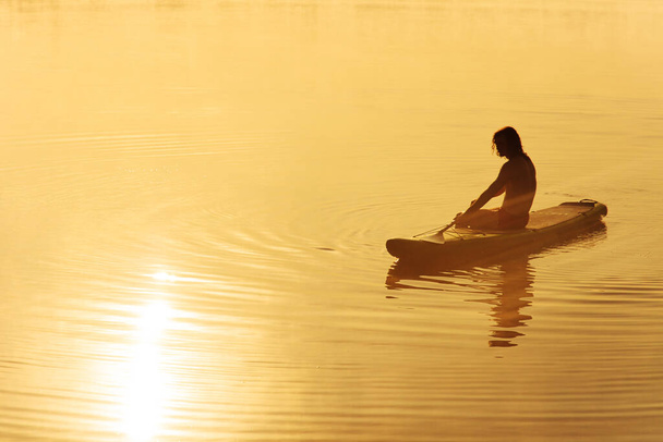 Mladý muž pádlo v siluetě relaxační na sup palubě - Fotografie, Obrázek