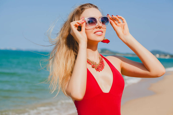 junge schöne blonde Frau sonnt sich am Strand in rotem Badeanzug, Sonnenbrille - Foto, Bild