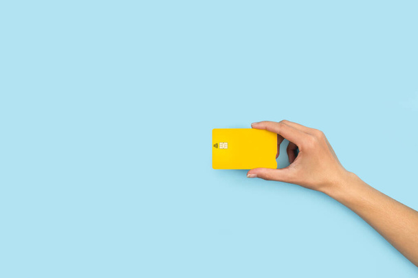Жінка рука тримає жовту кредитну картку на світло-блакитному тлі
 - Фото, зображення