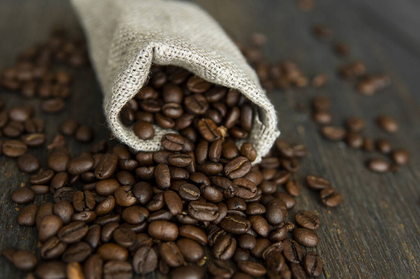 Coffee beans scattered from a linen bag on a wooden table. Fresh arabica coffee beans on linen textile. - Foto, Imagen