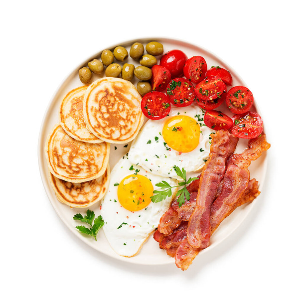Amerikkalainen aamiainen kahdella paistetulla munalla, pannukakulla, tomaattisalaatilla, pekonilla ja vihreillä oliiveilla. eristetty valkoisella pohjalla. ylhäältä - Valokuva, kuva