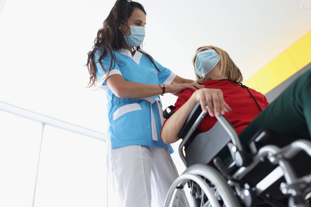 Physiotherapist doing back and shoulder massage to disabled young woman in wheelchair wearing protective medical masks - Foto, imagen