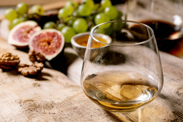 Glasses of red and white wine with grapes, figs, goat cheese and walnuts over old wooden background. Close up - Φωτογραφία, εικόνα