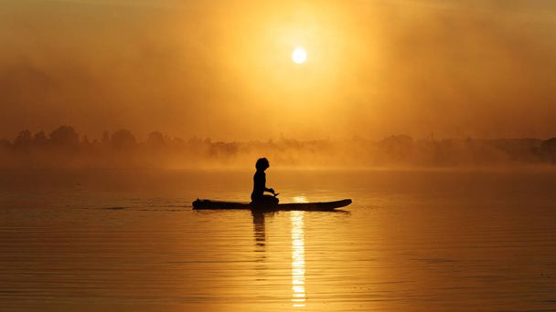 男がボード上に座って美しい日の出を楽しんで - 写真・画像