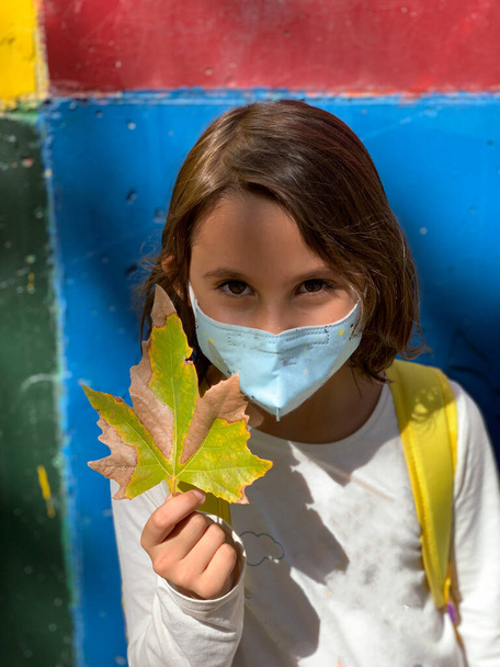 Κορίτσι με μάσκα, κράτα ένα φύλλο την φθινοπωρινή εποχή - Φωτογραφία, εικόνα