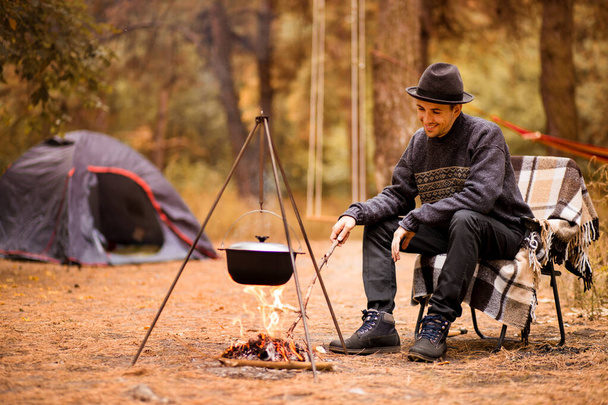Jovem acampando na tenda no dia de outono e cozinhe comida na fogueira. Conceito de férias - Foto, Imagem