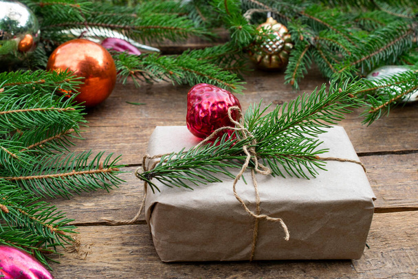 Karácsonyfa dekorációk és lucfenyő ágak újévi összetétele. Ajándék, kézműves papírba csomagolva egy lucfenyőből. Sötét fa textúra háttér. - Fotó, kép