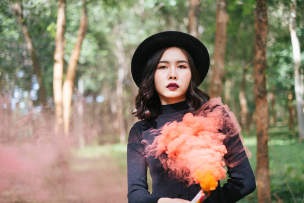 Une sorcière robe noire jouant des torches de fumée orange dans la forêt. - Photo, image