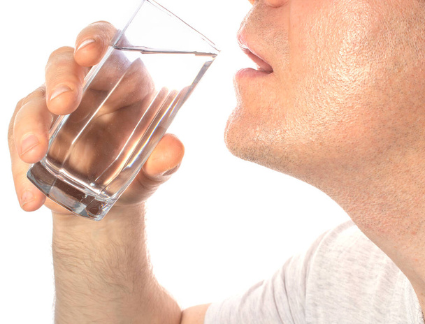 a man brings a glass cup of clean water to his mouth, on white background. the concept of taking medicine inside, quenching his thirst. copy space. - Foto, afbeelding