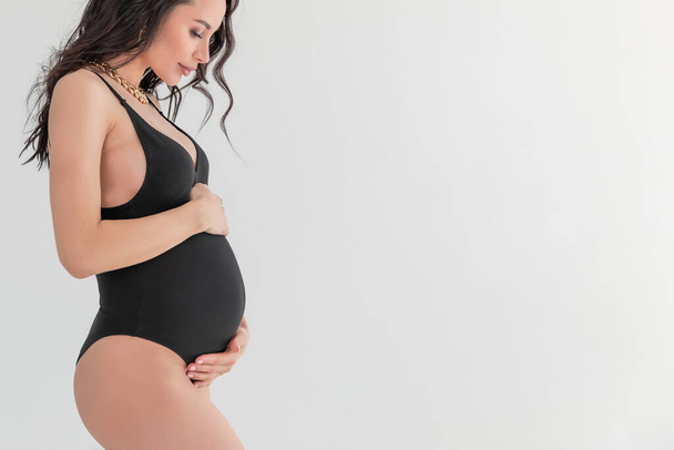 A fashion stylish pregnant sexual woman in Vogue style. beautiful Girl with belly for 9 months waiting for baby. On a white gray background. glamorous Pregnant in a black bodiesuit. Copy space - Foto, Imagem