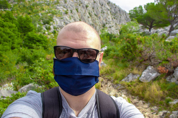 A kopasz férfi fekete napszemüveget visel, és egy kék arcmaszkot, ami szelfit készít túrázás közben, túrázva a természetben Horvátországban. A természet felfedezése ősszel a világjárvány idején - Fotó, kép