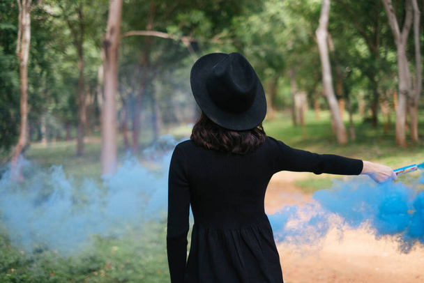 Eine schwarze Hexe spielt blaue Rauchfackeln im Wald. - Foto, Bild
