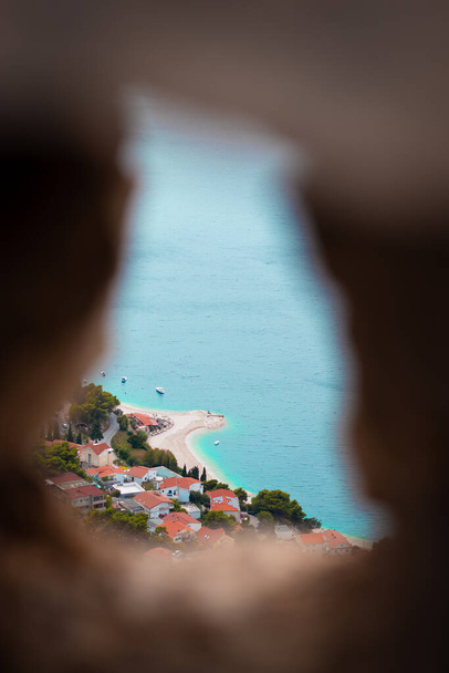 Vertikale Aufnahme eines Strandes in der Stadt Omis, Kroatien, von der Bergspitze aus gesehen, eingerahmt zwischen den Steinmauern der Burg Fortica - Foto, Bild