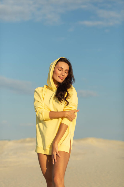 A young beautiful girl with a good figure, around only white sand and blue sky, she is wearing a yellow sweater - Fotografie, Obrázek