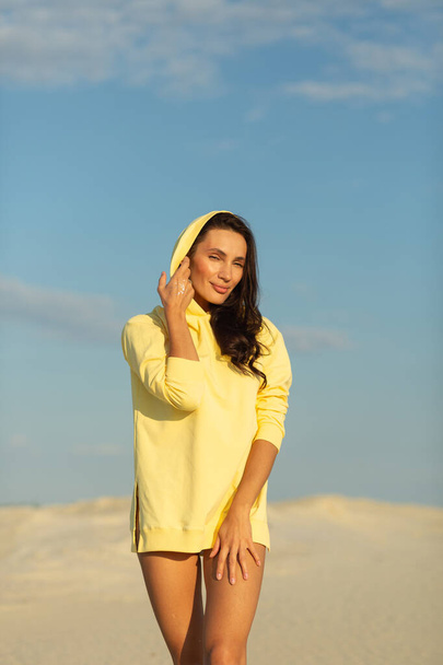 A young beautiful girl with a good figure, around only white sand and blue sky, she is wearing a yellow sweater - Foto, imagen