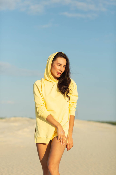 A young beautiful girl with a good figure, around only white sand and blue sky, she is wearing a yellow sweater - Foto, immagini