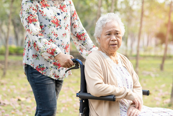 Азиатская пожилая женщина или пожилая женщина улыбается светлое лицо пациента на инвалидной коляске в парке. - Фото, изображение