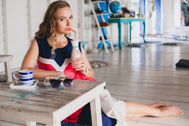 young stylish beautiful woman in sea cafe, drinking cocktail smoothie, sunglasses, flirty, resort style, fashionable outfit, smiling, marine colors dress - Foto, afbeelding