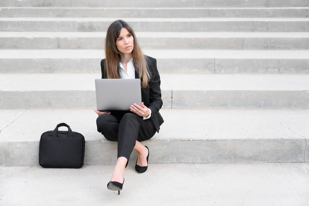 Jeune femme d'affaires utilisant un ordinateur portable en ville, assise sur un escalier. - Photo, image