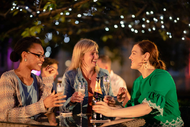 Bir grup farklı bayan arkadaş bir bar / restoranda şampanya içiyor, kutlama yapıyor ve birlikte eğleniyorlar.. - Fotoğraf, Görsel