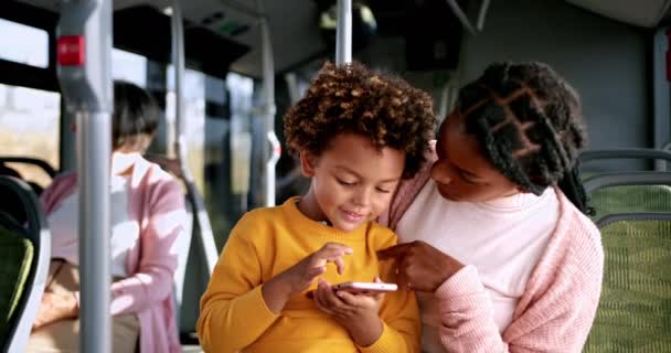 African-american boy playing with phone on mother lap inside bus - Video