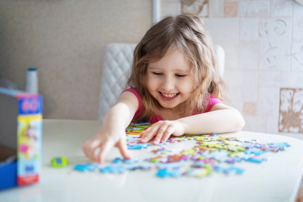 little girl with light wavy hair collects a puzzle at home and has fun. The child collects a picture from the details. Development of thinking. - 写真・画像