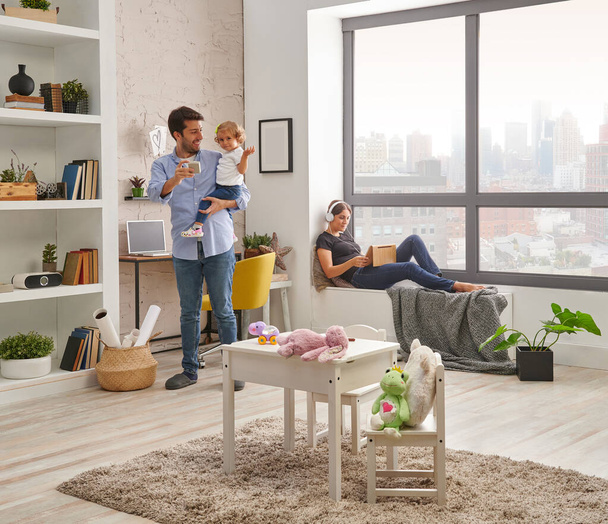 Papá, mamá y el bebé pasan un buen rato en casa, trabajando, mirando tableta en la sala de estar. pared decorativa moderna y estilo interior. - Foto, Imagen