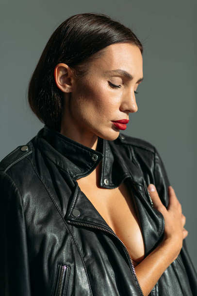 Young beautiful girl with a good figure, in glasses and in a black leather jacket, with a naked body in the studio on a white background - Foto, immagini