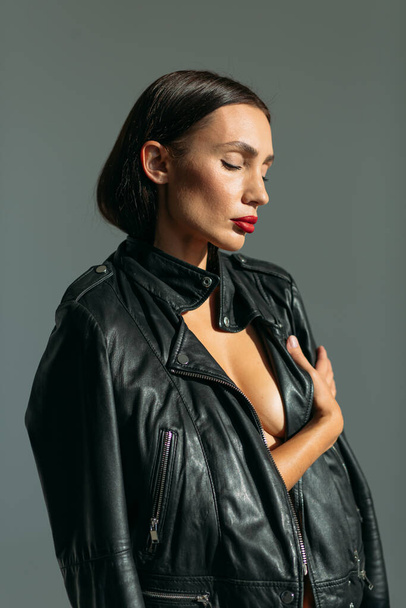Young beautiful girl with a good figure, in glasses and in a black leather jacket, with a naked body in the studio on a white background - Fotografie, Obrázek