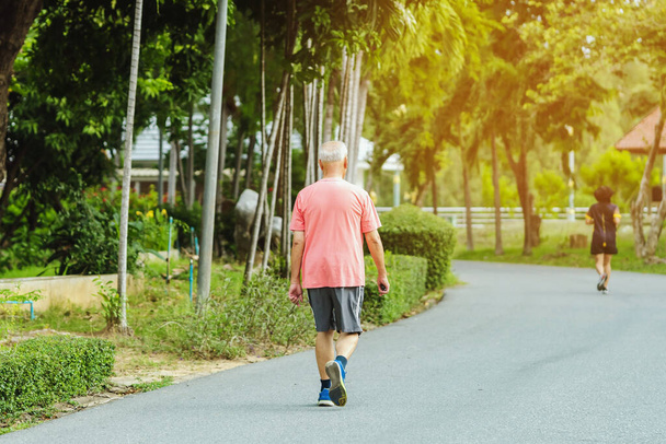Rückenansicht Porträt eines asiatischen älteren Mannes in Fitnessbekleidung beim Gehen und Joggen für eine gute Gesundheit im öffentlichen Park. Senior Jogger in der Natur. Älterer Mann genießt friedliche Natur. Gesundheitskonzept. - Foto, Bild