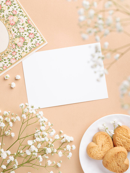 Papelería romántica plana con tarjeta de felicitación en blanco y flores blancas sobre fondo beige - Foto, Imagen