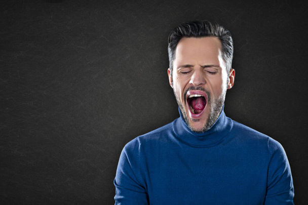 Young man in a blue pullover yawning tired and bored - Photo, Image