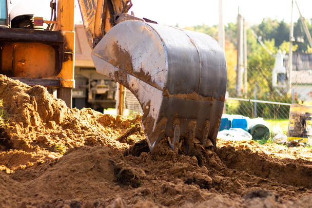 Металлическое ведро экскаватора копает песок или глину на строительной площадке, выкапывая траншею. - Фото, изображение