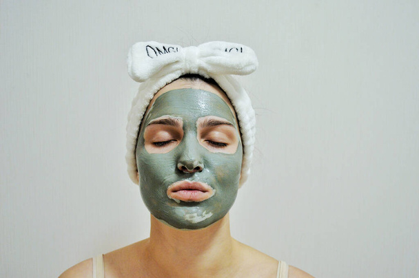 Menina com uma bandagem na cabeça e uma máscara de barro em seu rosto em um fundo branco - Foto, Imagem
