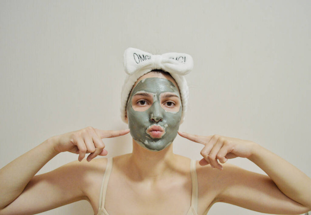 Meisje met een verband op haar hoofd en een klei masker op haar gezicht op een witte achtergrond - Foto, afbeelding