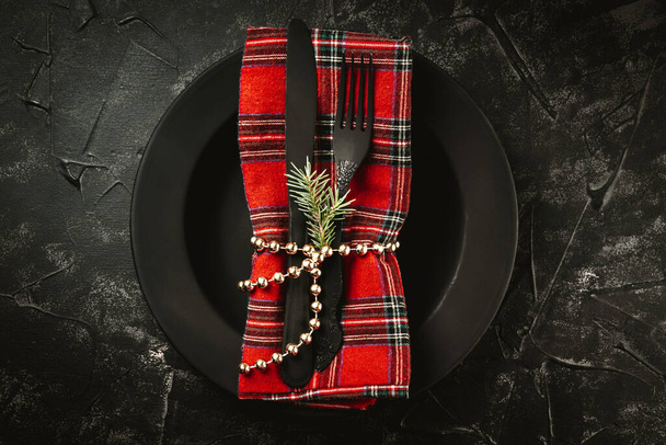  Black cutlery on red napkin and black plate - minimalistic dark christmas background. New Year's table setting in black. High quality photo - Photo, image